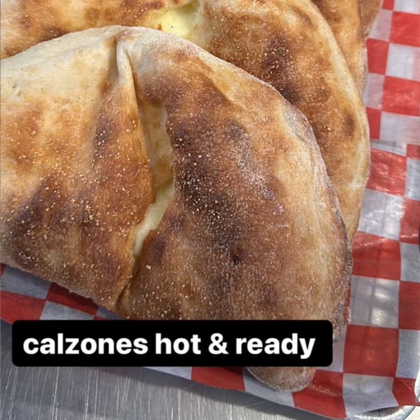Golden-brown calzones with melted cheese filling, served on red and white checkered paper.