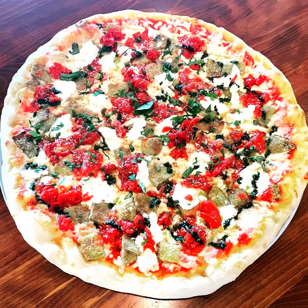 Mamma Mia's pizza with red sauce, white cheese, green herbs, and sausage on a wooden table.