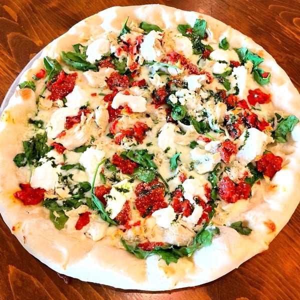 Mamma Mia's white pizza with chicken, sun-dried tomatoes, ricotta, and spinach on a wooden table.